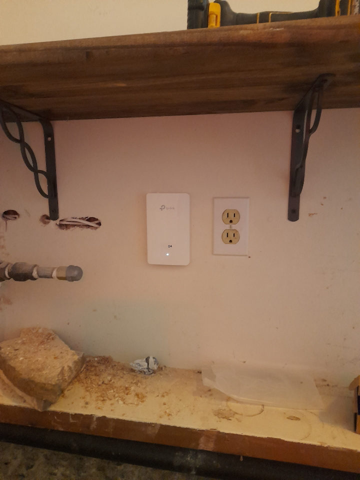 Wall-mounted network adapter next to a power outlet under a wood shelf.
