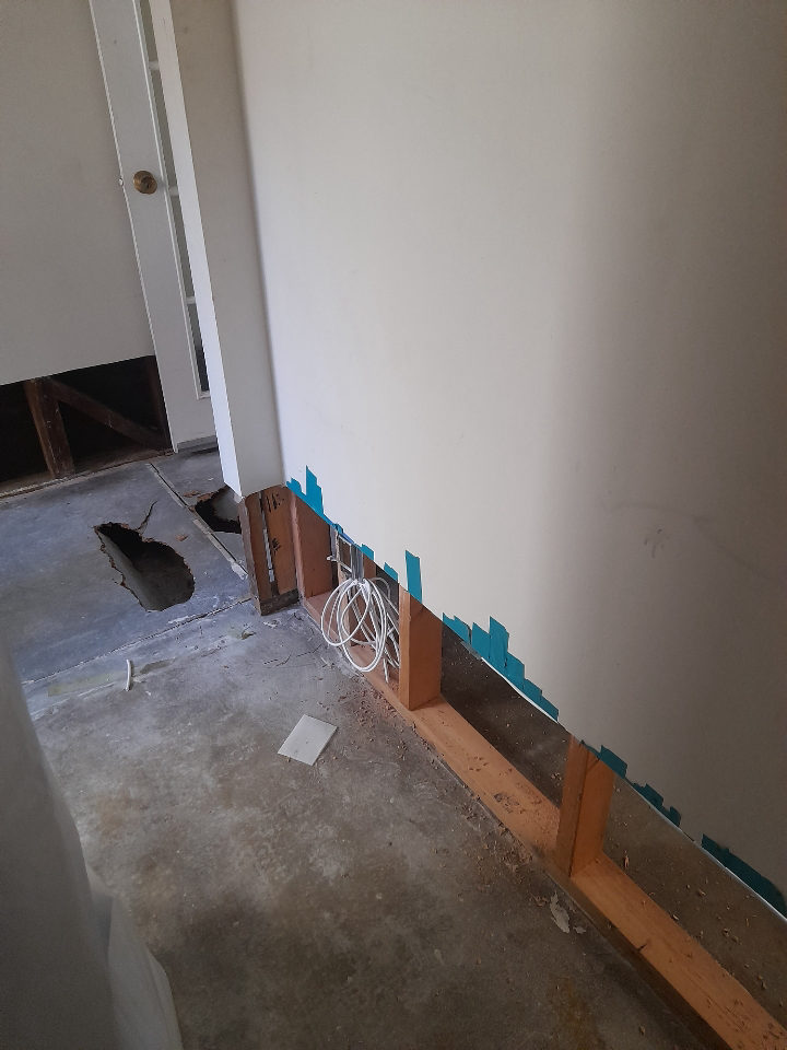 Ethernet cable coiled with service slack inside an open lower-level wall cavity during construction., white cable in stud bay