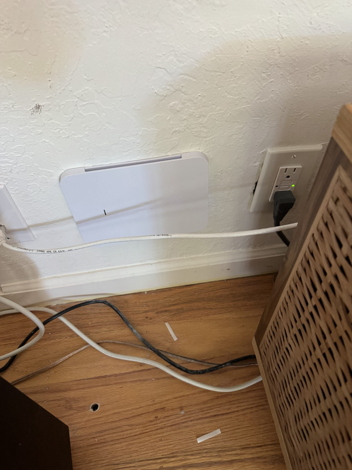 Access point cover at baseboard level near an outlet and cords.