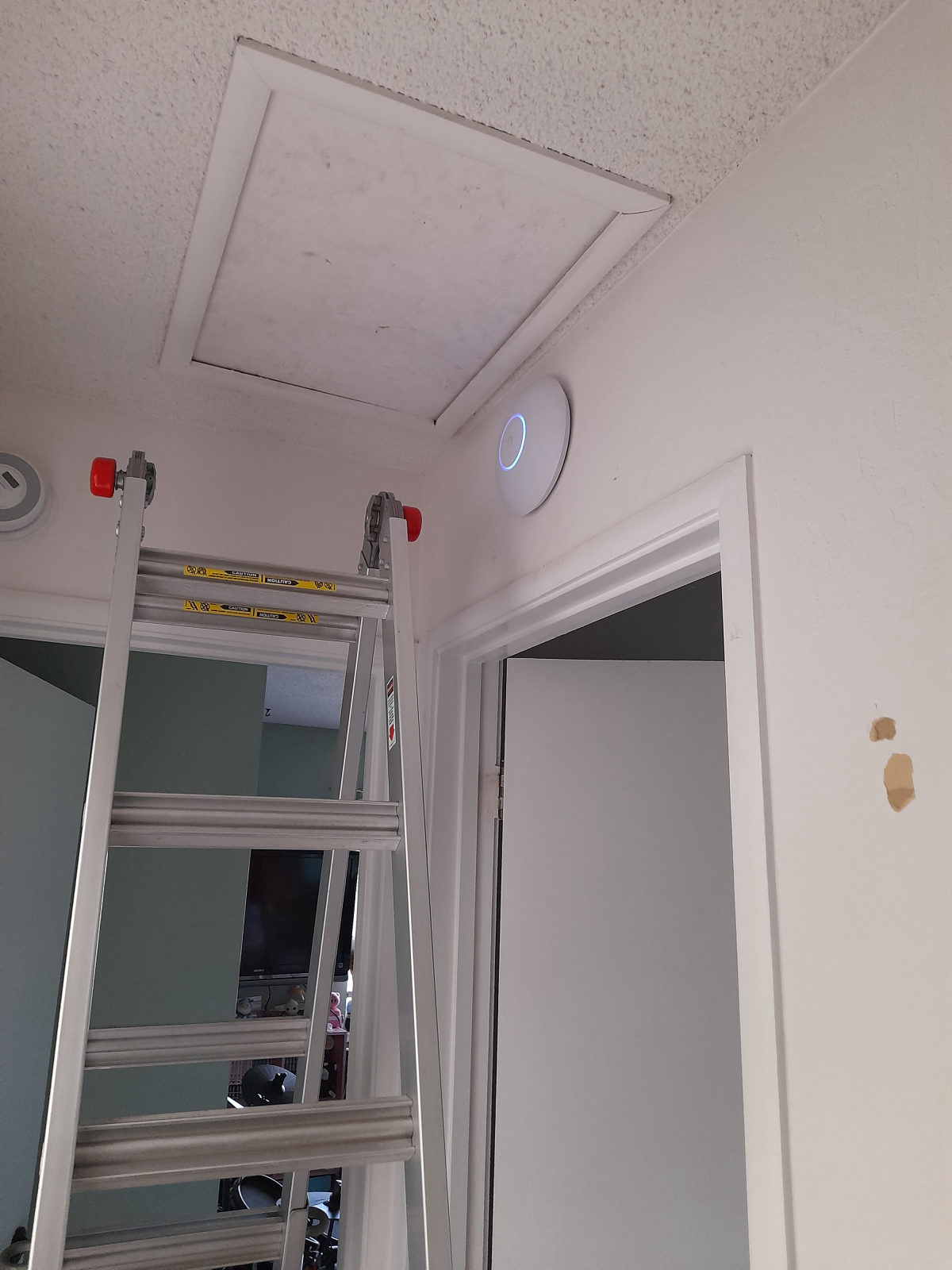 Ubiquiti ceiling access point mounted above a doorway beside an attic hatch