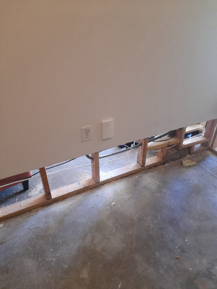 Ethernet cable routed through open wall framing up to a flush wall plate beside an outlet.